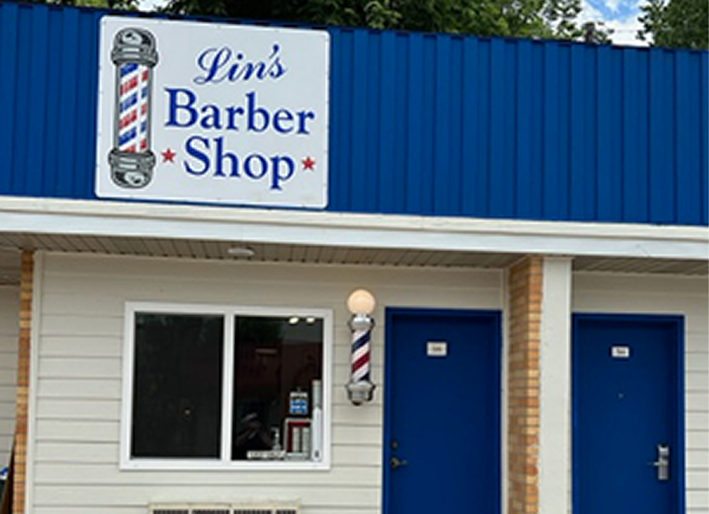 Image of Lin holding a 2020 South Dakota Barber of the Year Trophy while smiling in his barber shop